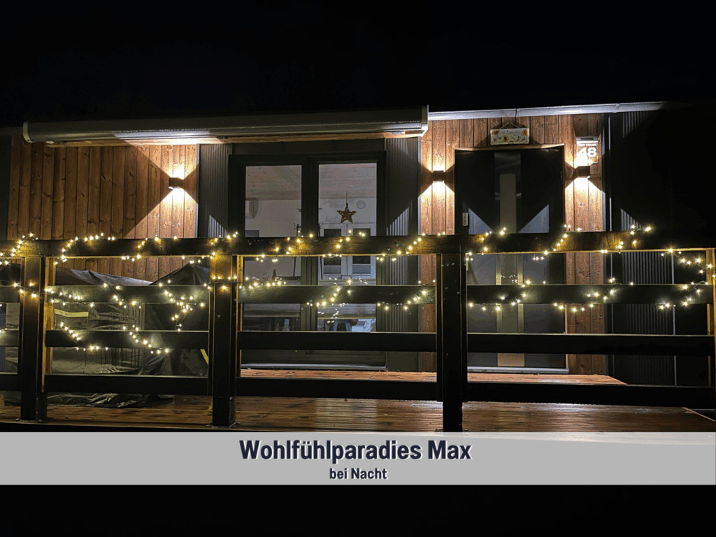 Tiny House Max im Wohlfühlparadies Max & Moritz bei Nacht – stimmungsvolle Beleuchtung und Lichterkette auf der Terrasse am Plauer See sorgen für gemütliche Abendatmosphäre.
